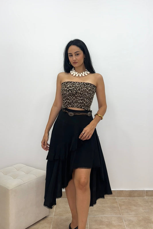 A woman modeling a strapless tube top with a leopard print pattern and a black high-low skirt, accessorized with a chunky white statement necklace and a black belt.